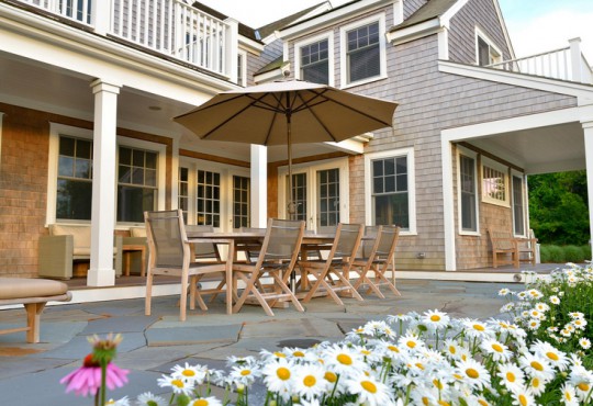 Barlow Tyrie Oval Teak Wood Dining Table, accompanied by eight dining chairs and an umbrella